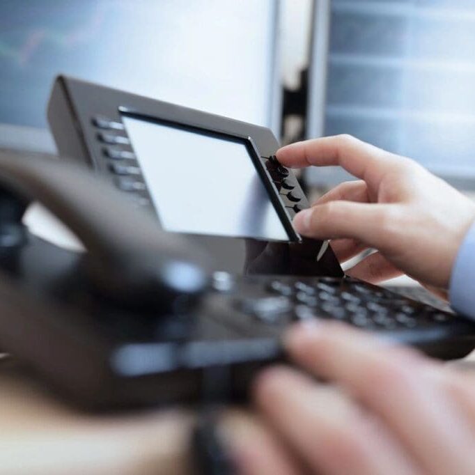 Hand pressing buttons on a business VoIP desk phone with touchscreen display